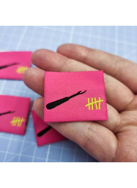 A hand holding out a hot pink woven sew-in label with a black seam ripper